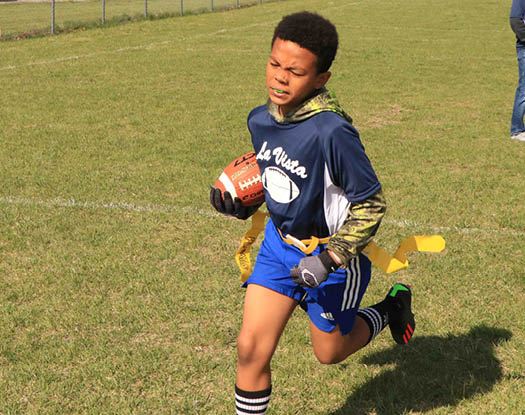 Boy wearing a La Vista football jersey and running with a football